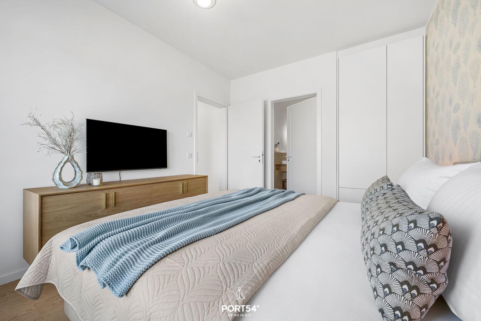 Bedroom with bed, TV, and closet. Wall with pattern. Duvet and pillow with patterns.