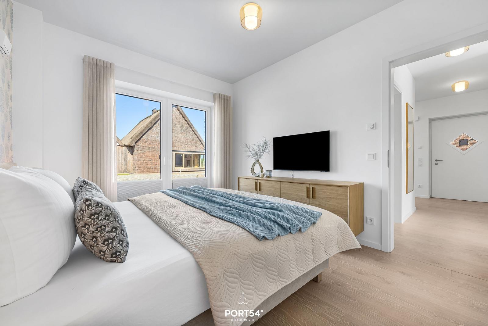 Bedroom with bed, TV, and view of thatched roofs through window.