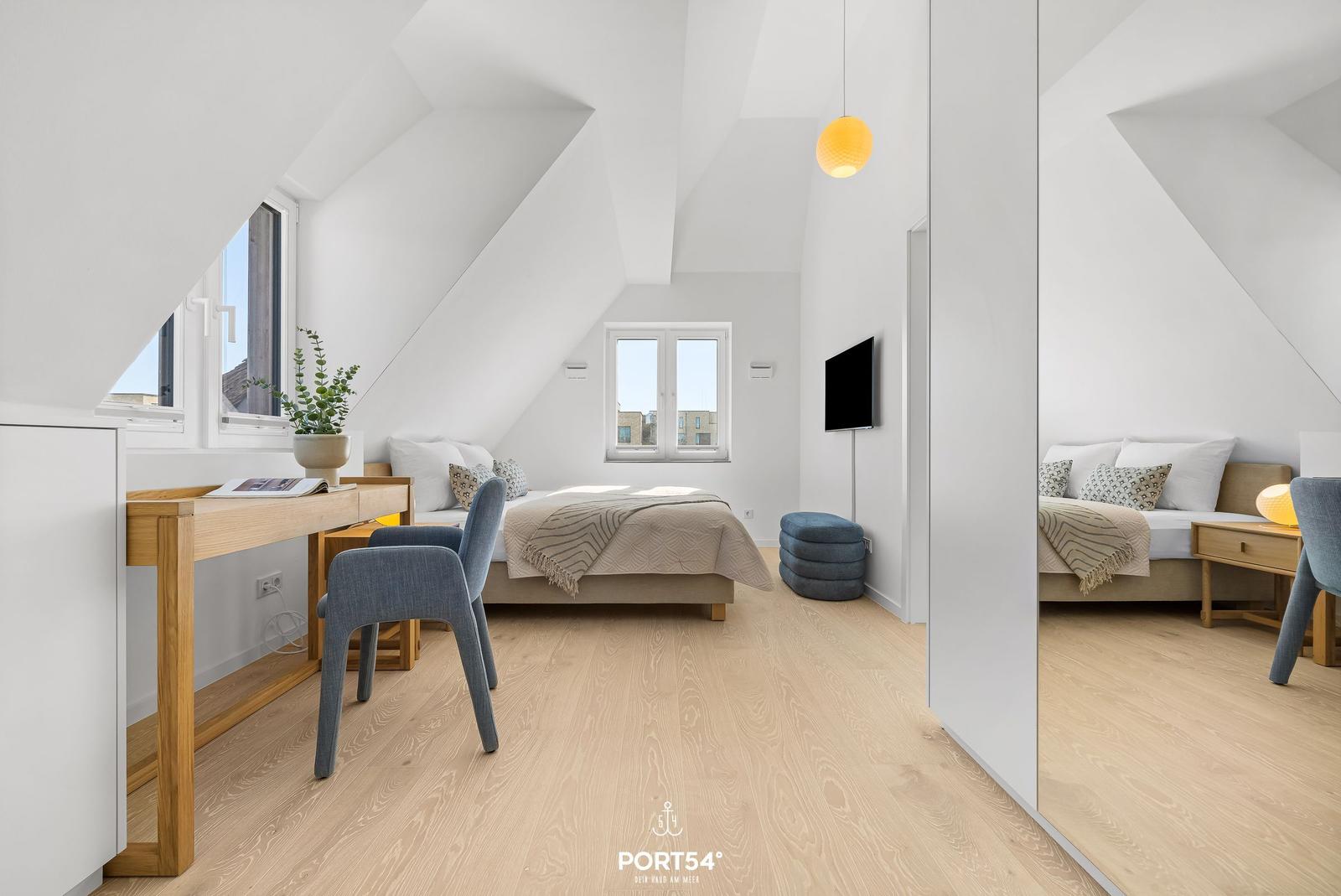 Bedroom with sloped ceilings, bed, desk, and windows.