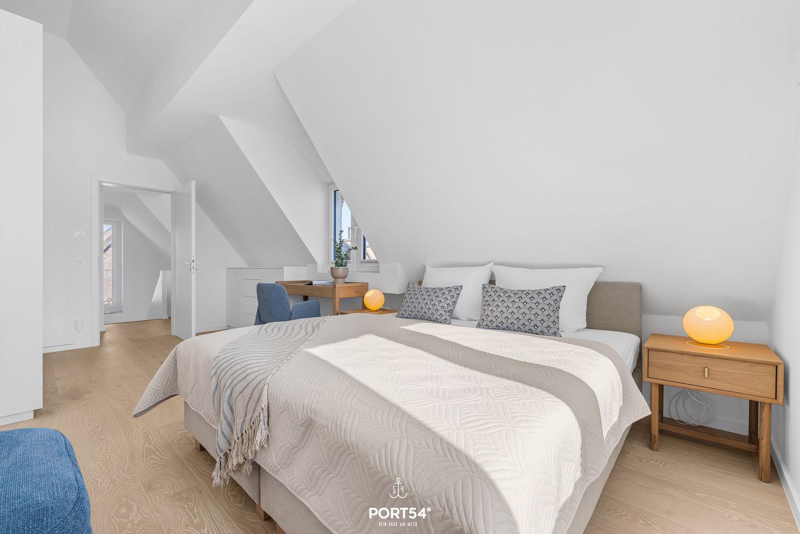 Bedroom with sloped ceiling, bed, nightstand, and desk.