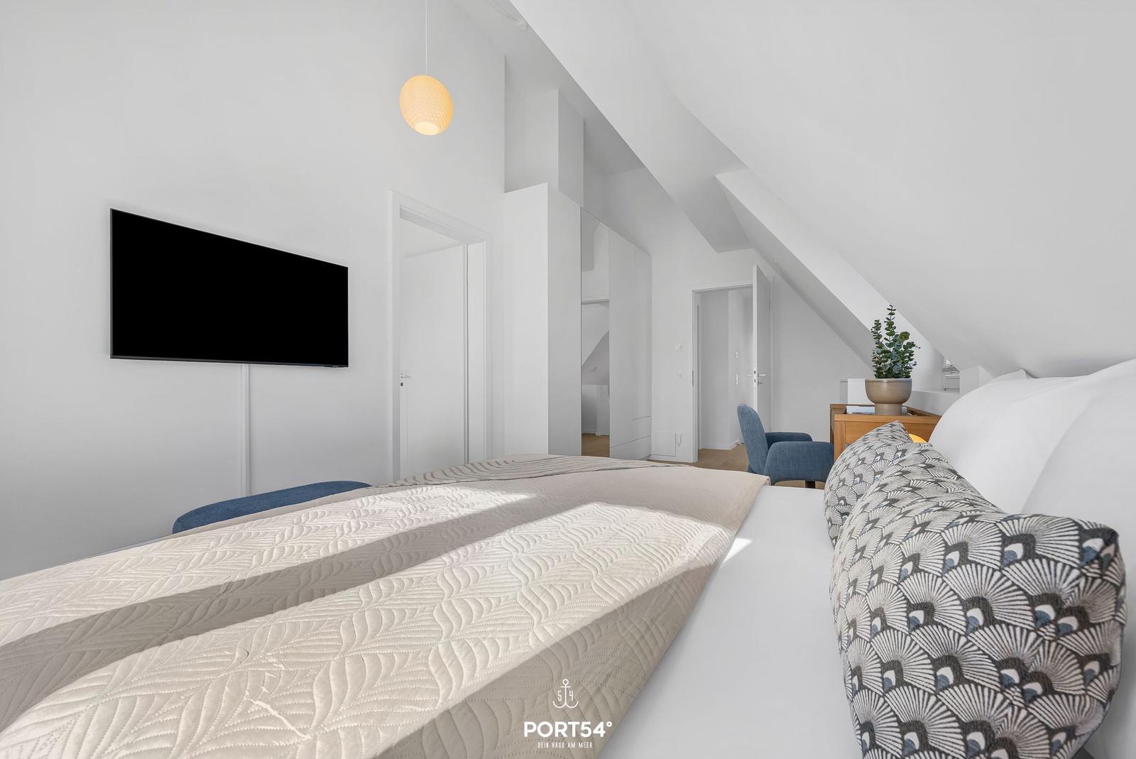 Bedroom with sloped ceiling, bed, TV, and seating area.