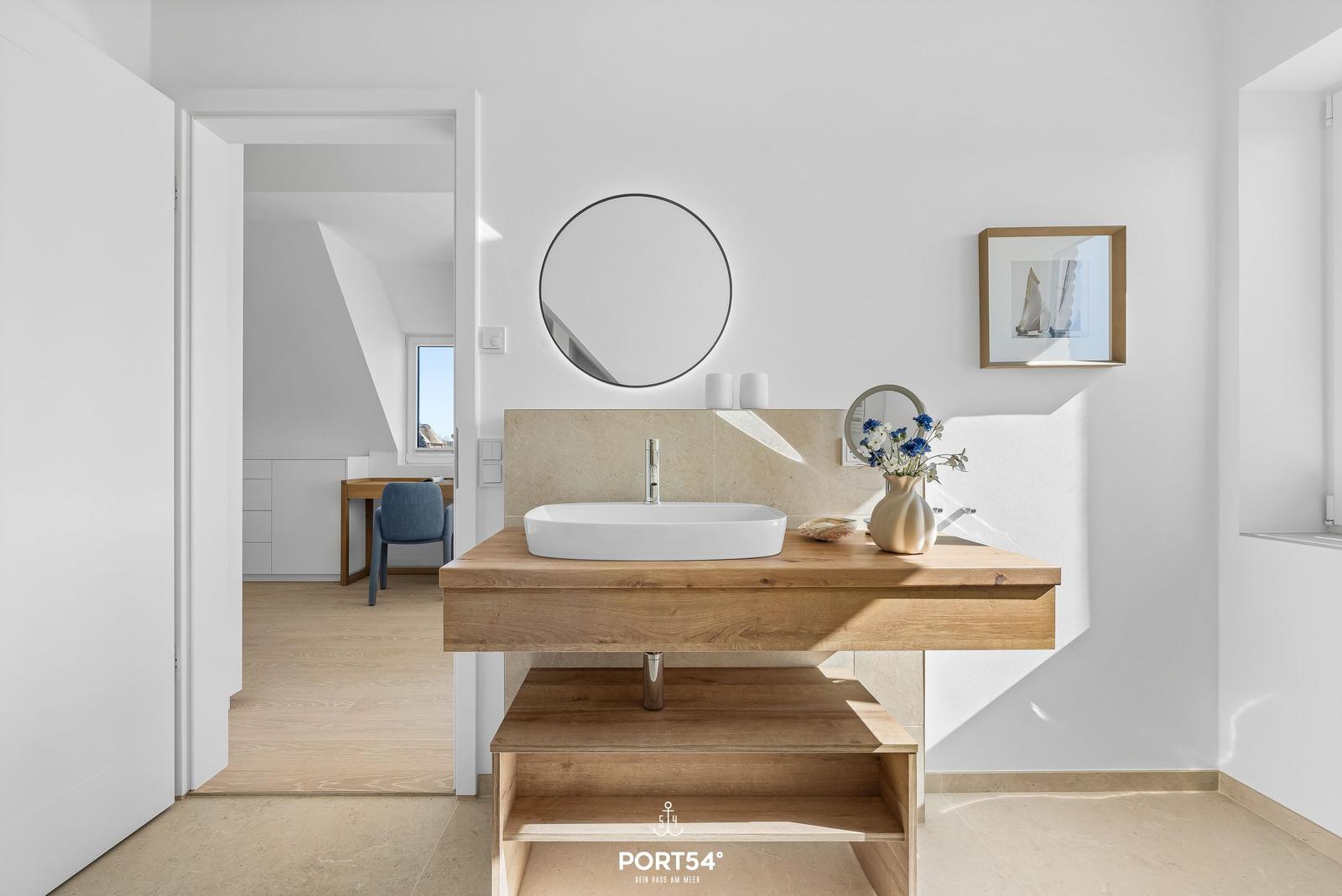 Bathroom with wooden vanity, round mirror, and flowers.