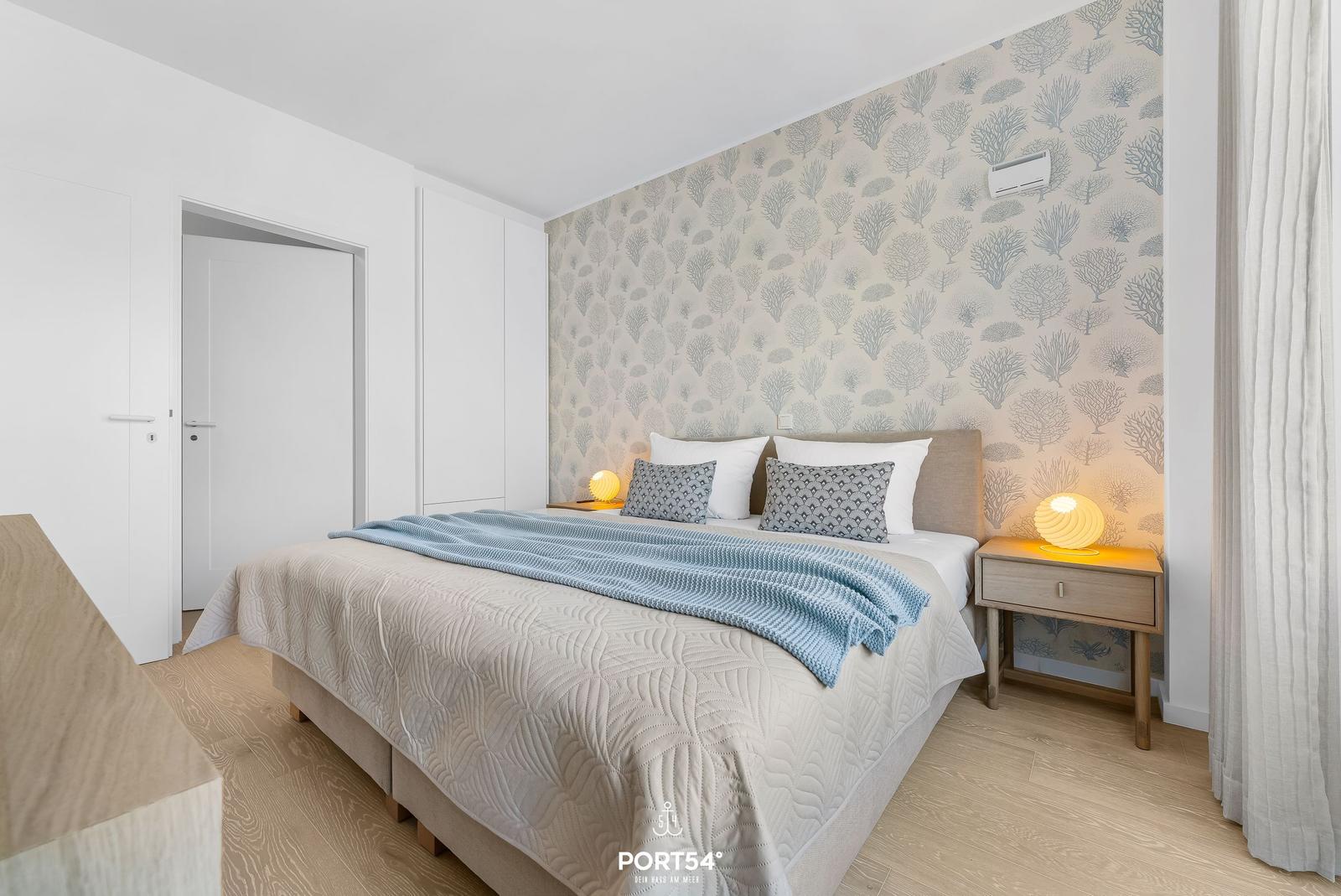 Bedroom with bed, nightstand, and patterned wallpaper.