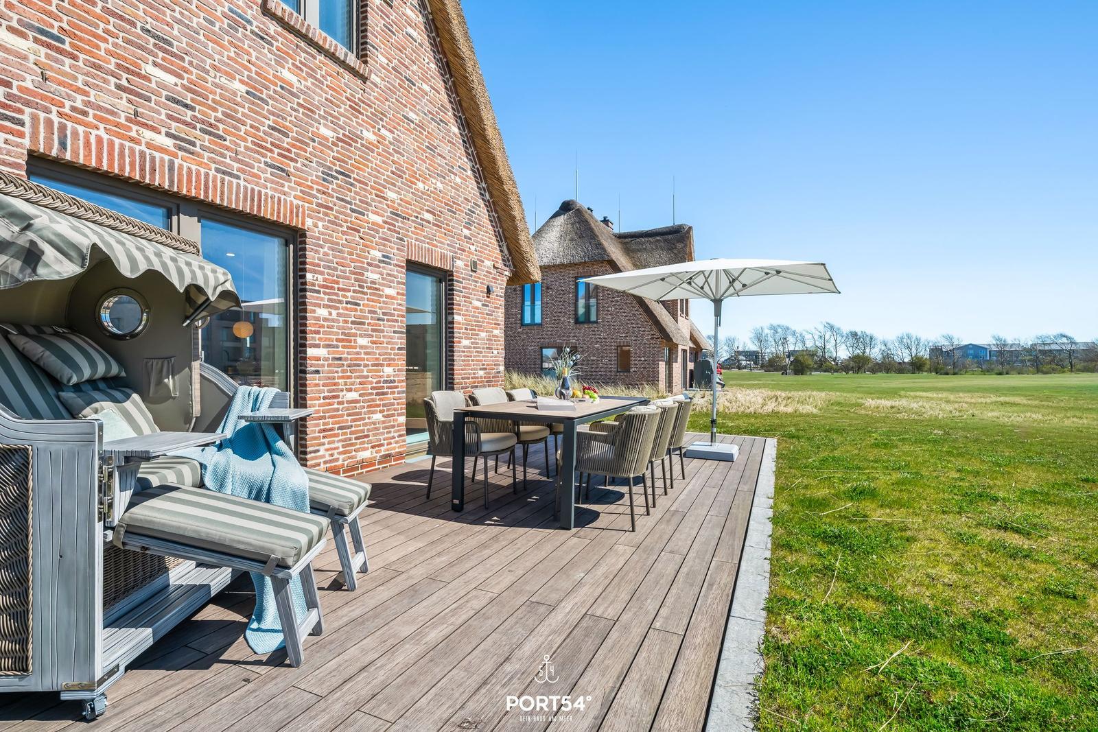 Deck with seating, table, and umbrella next to a brick house.