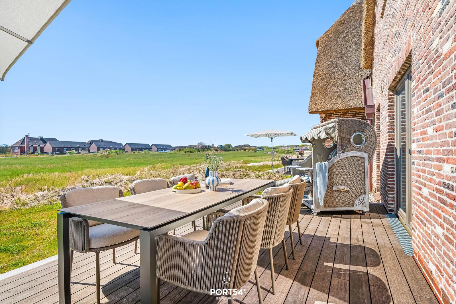Terrace with table and chairs, view of fields and buildings.