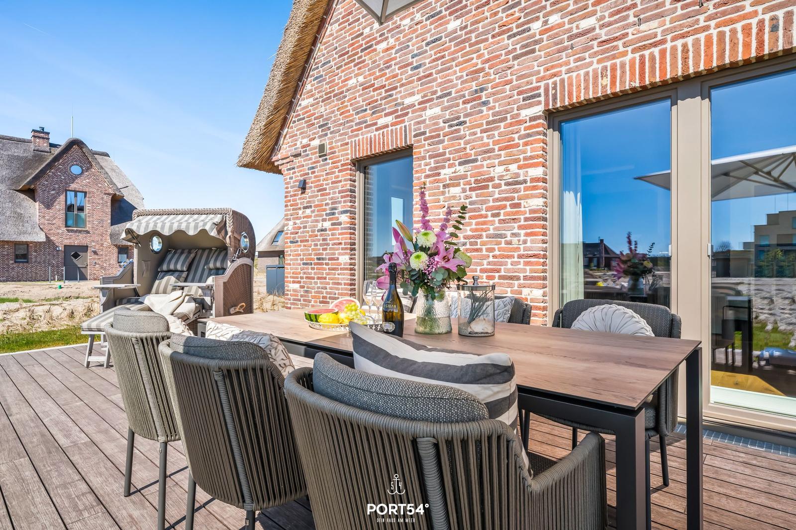 Terrasse mit Esstisch, Stühlen und Blick auf Backsteinhaus.