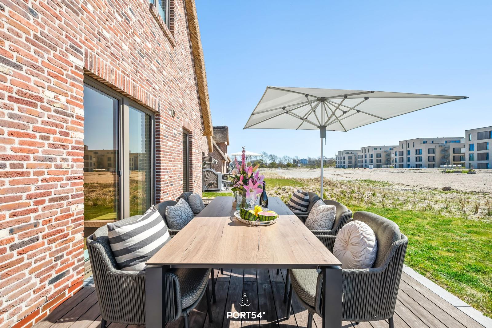 Terrasse mit Tisch, Stühlen und Sonnenschutz neben Backsteinhaus.
