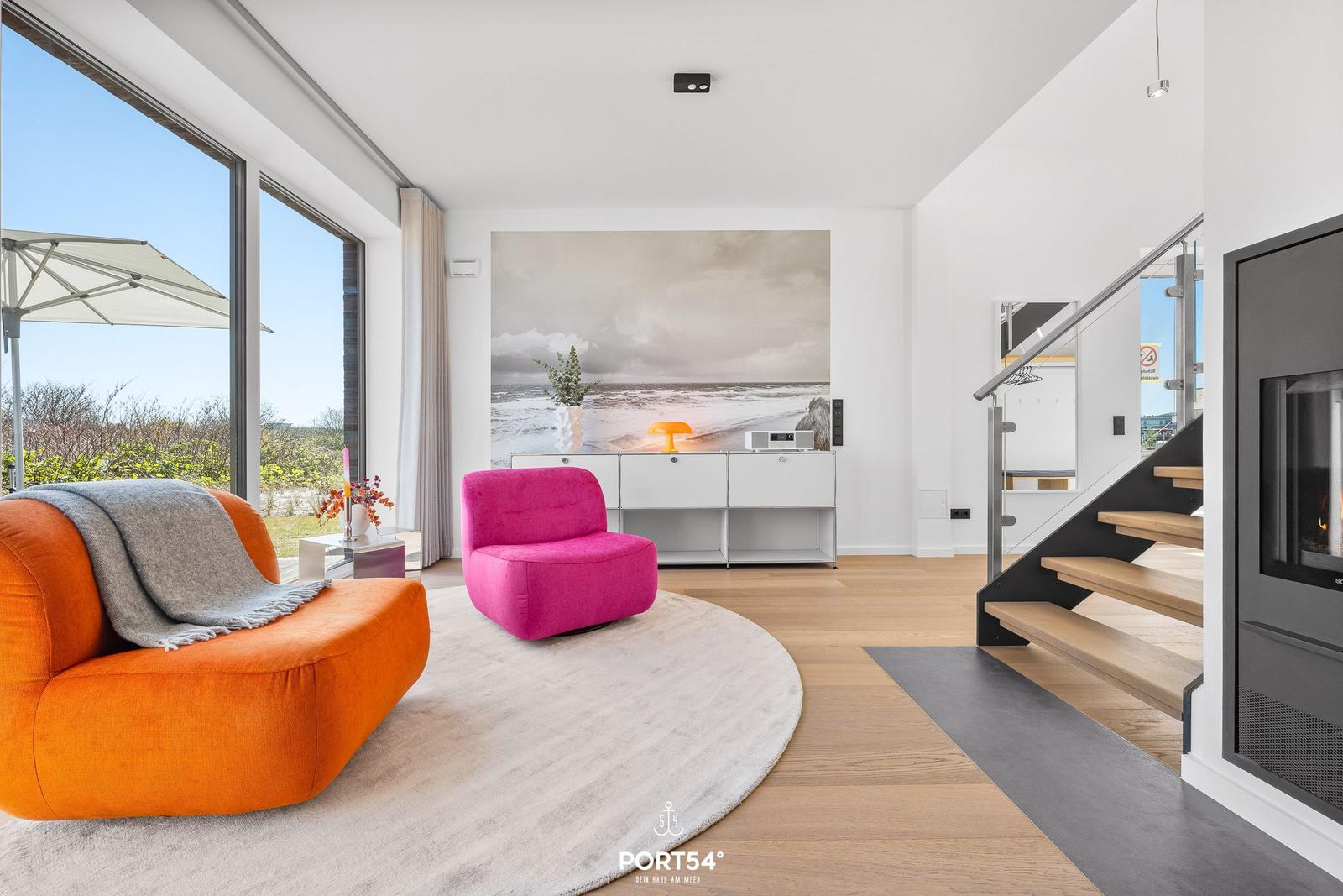 Wohnzimmer mit orangefarbenem Sofa, pinkem Sessel und Blick auf den Garten.