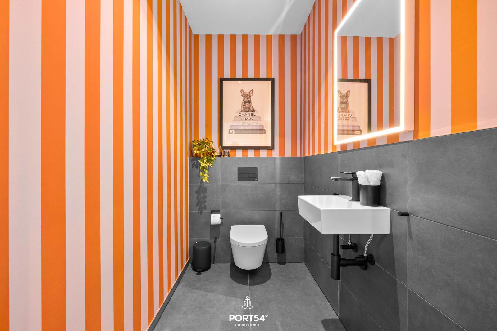 Badezimmer mit orangefarbenen Streifen an den Wänden und grauen Fliesen.