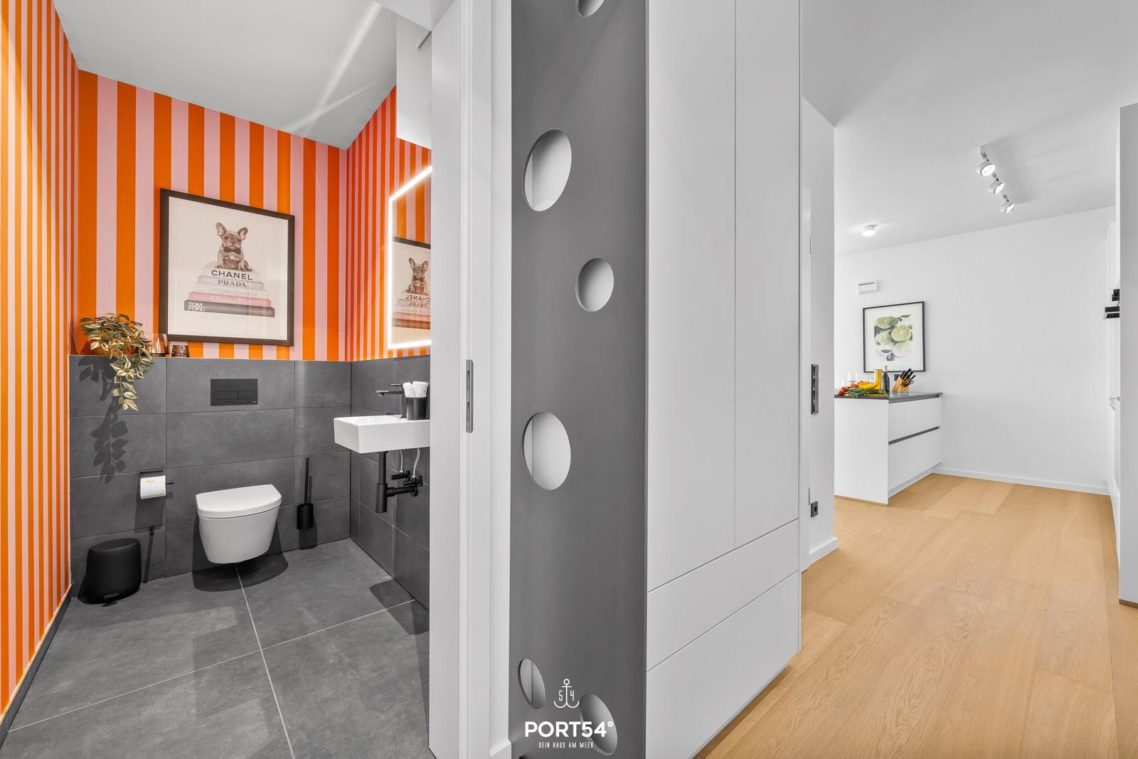 Badezimmer mit orangefarbenen Streifen und moderner Einrichtung. Blick in die Küche.