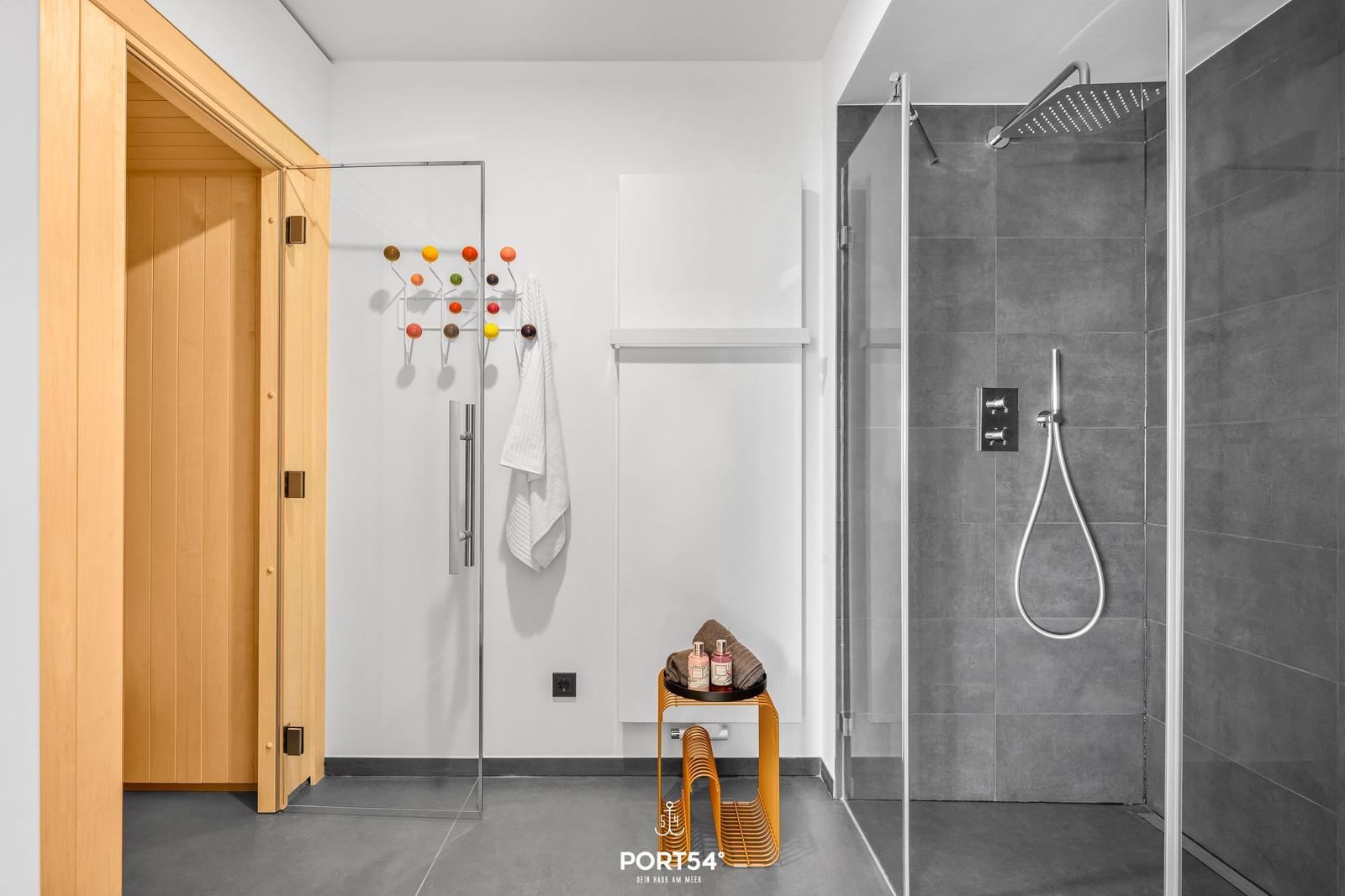 Dusche mit Regenduschkopf, Sauna und Handtuchständer mit bunten Haken.