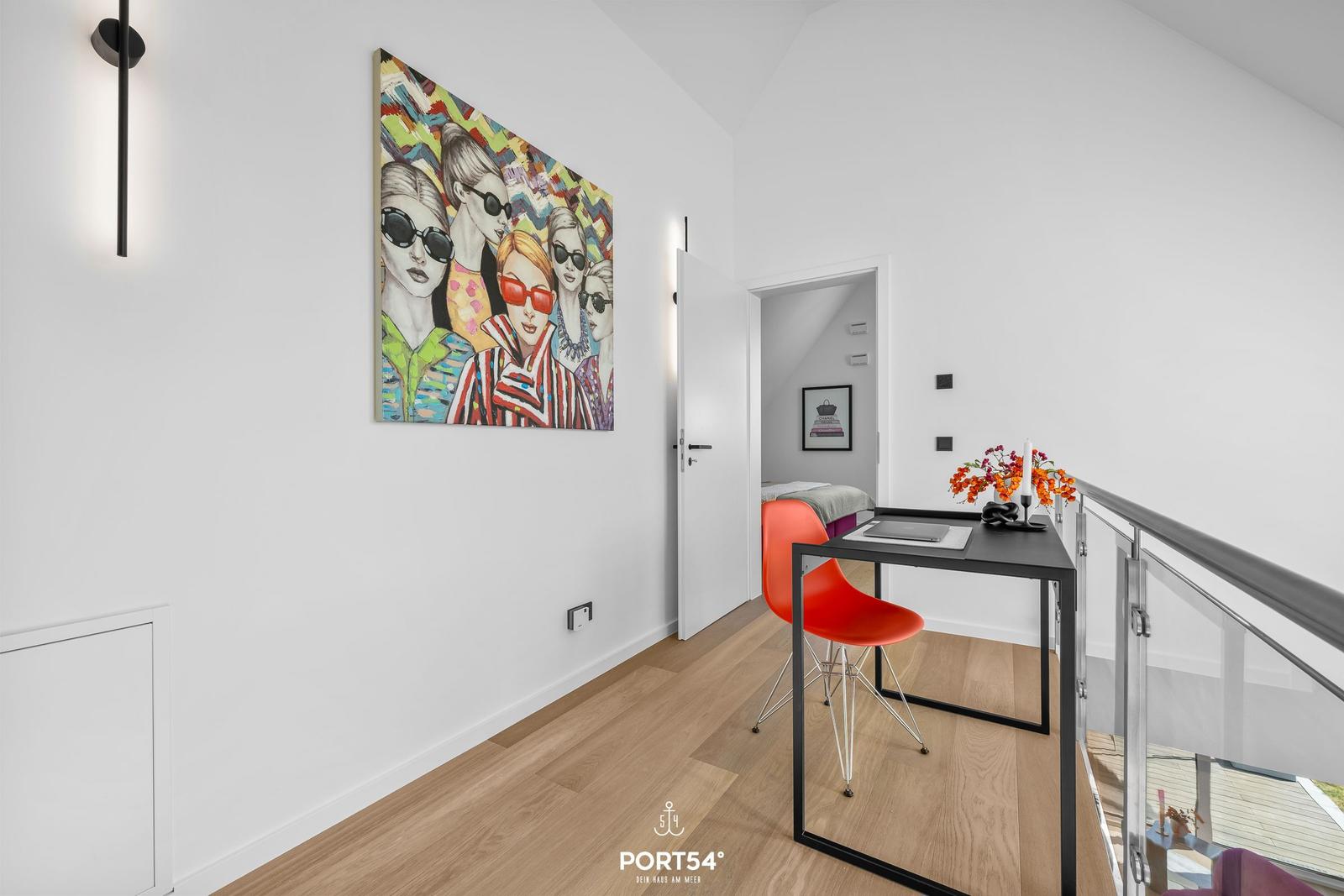 Schlafzimmer mit Schreibtisch, roter Stuhl und Wandbild.