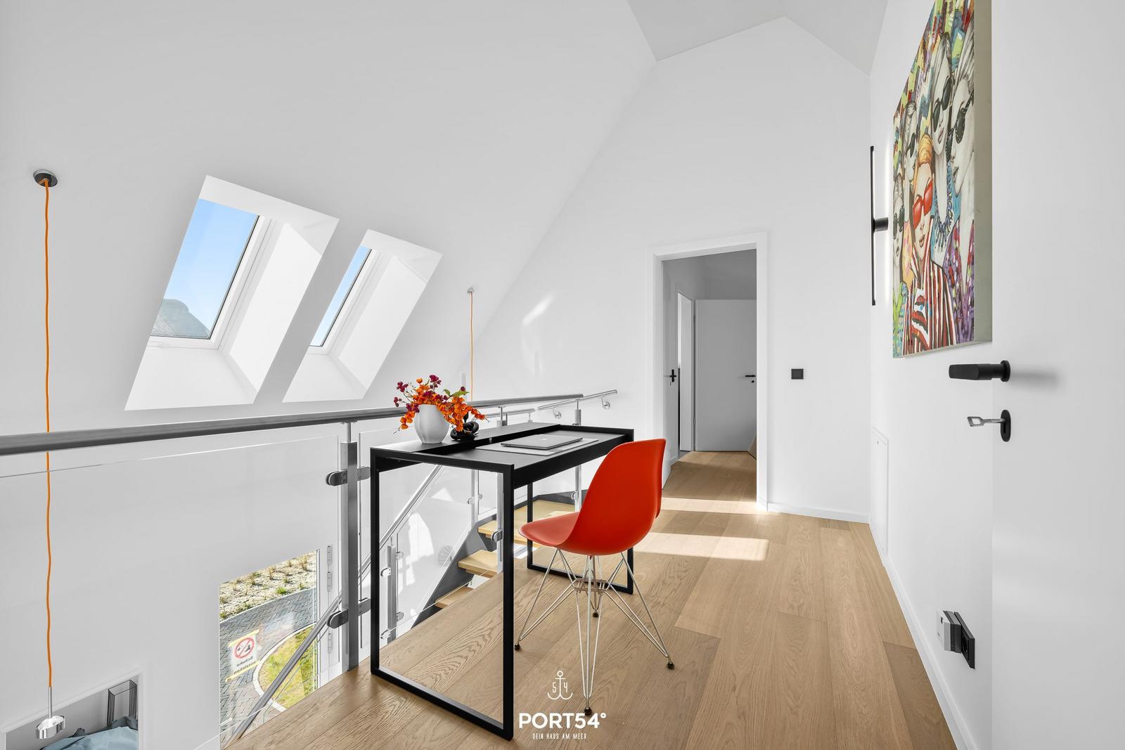 Schlafzimmer mit Dachfenstern, Schreibtisch und roter Stuhl.