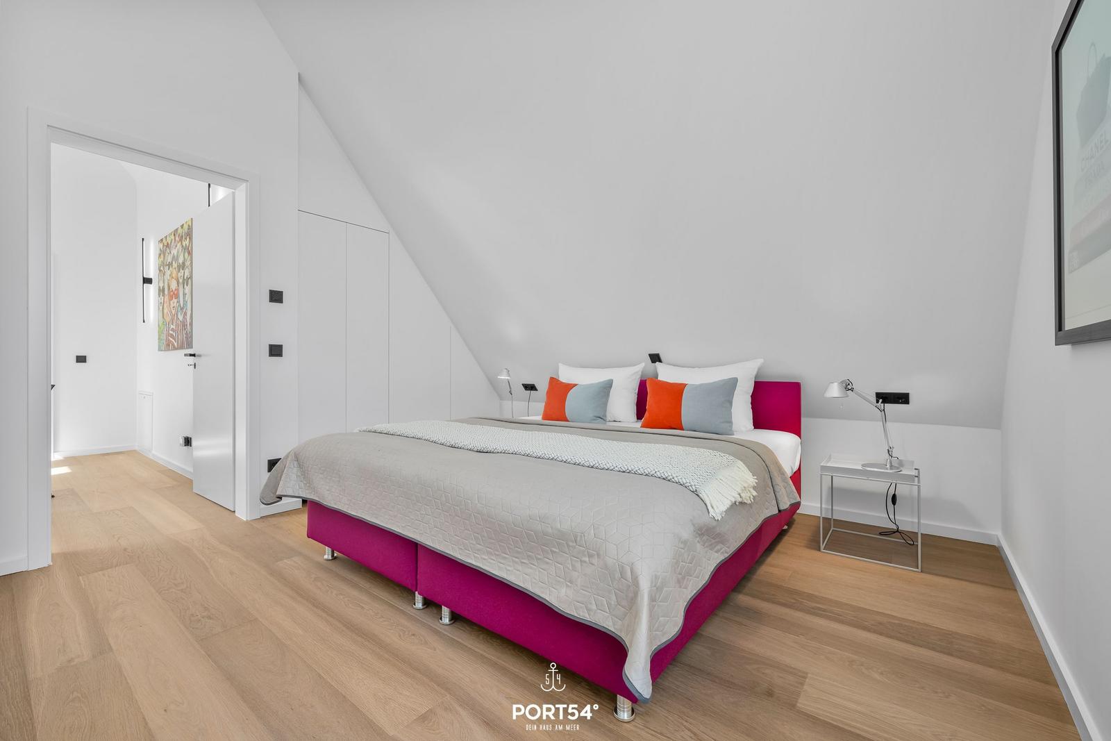 Schlafzimmer mit pinkem Bett und Holzboden unter schräger Decke.