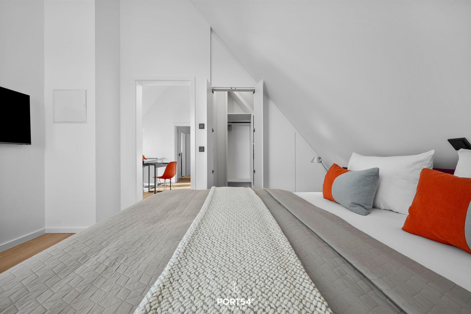 Schlafzimmer mit Dachschräge, Bett mit Kissen und TV an der Wand.