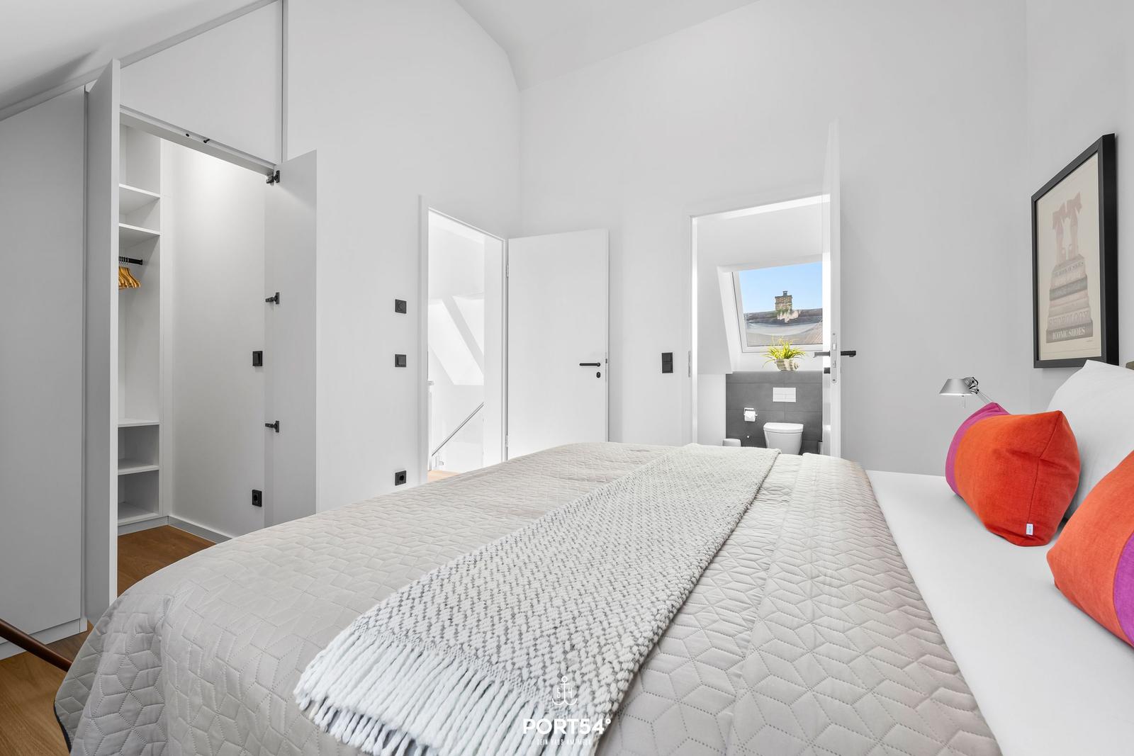 Schlafzimmer mit Bett, Kleiderschrank und Blick auf Bad.