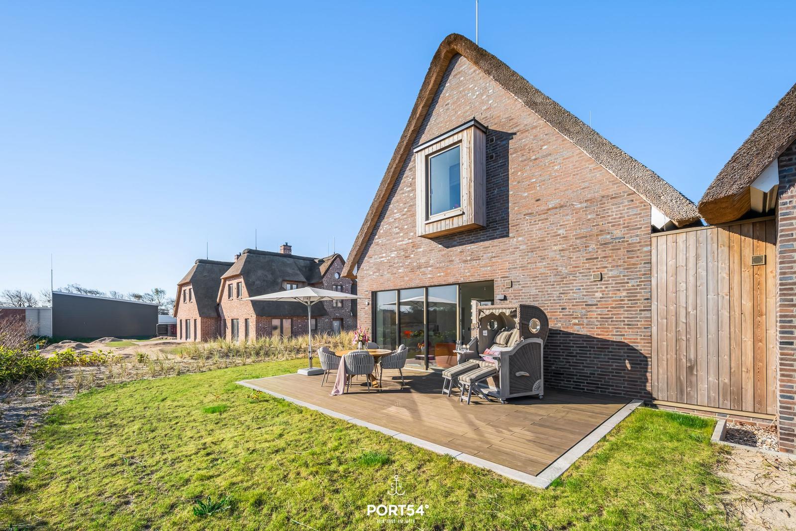 Haus mit Dach aus Stroh und Terrasse mit Sitzgelegenheiten.