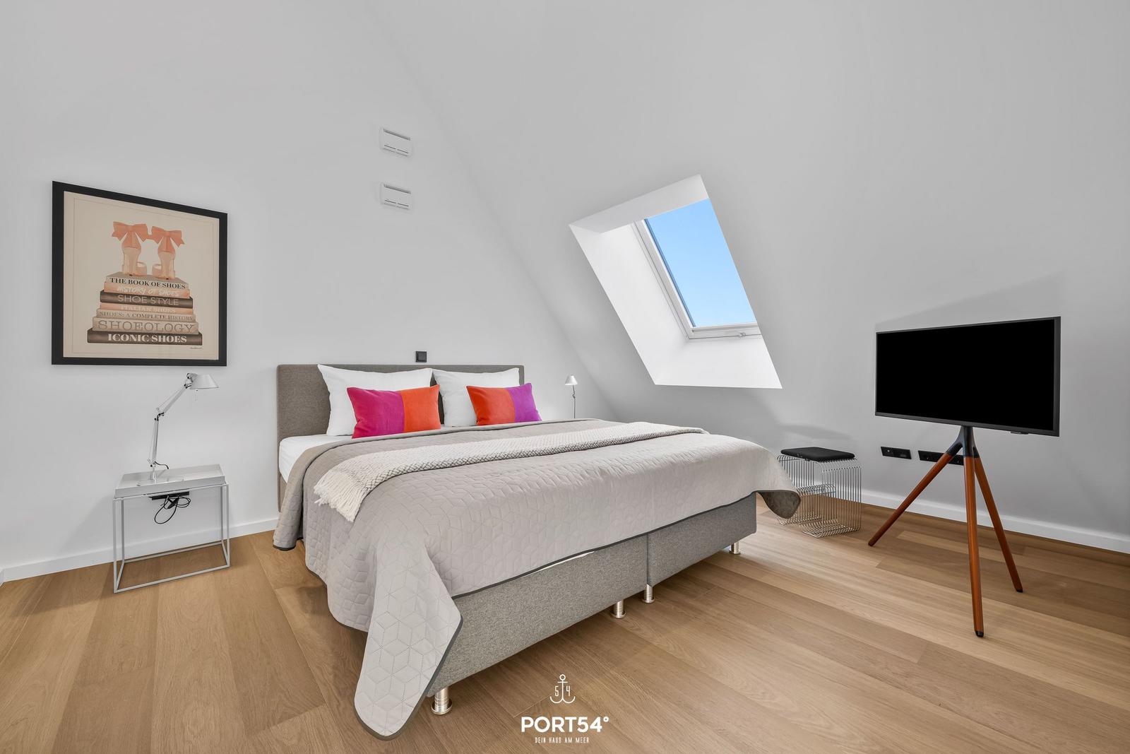 Schlafzimmer mit Dachfenster, Bett, TV und Nachttisch.