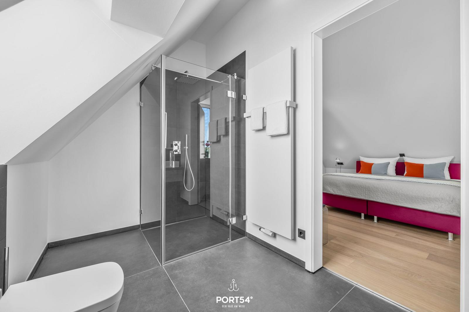 Badezimmer mit Dusche und angrenzender Schlafzimmer mit Bett.