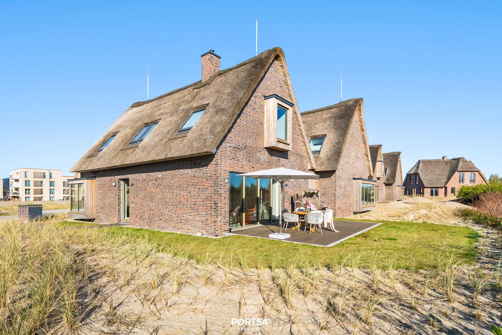 Haus mit Strohdach, Terrasse und Garten. Modernes Design mit Holz und Glas.