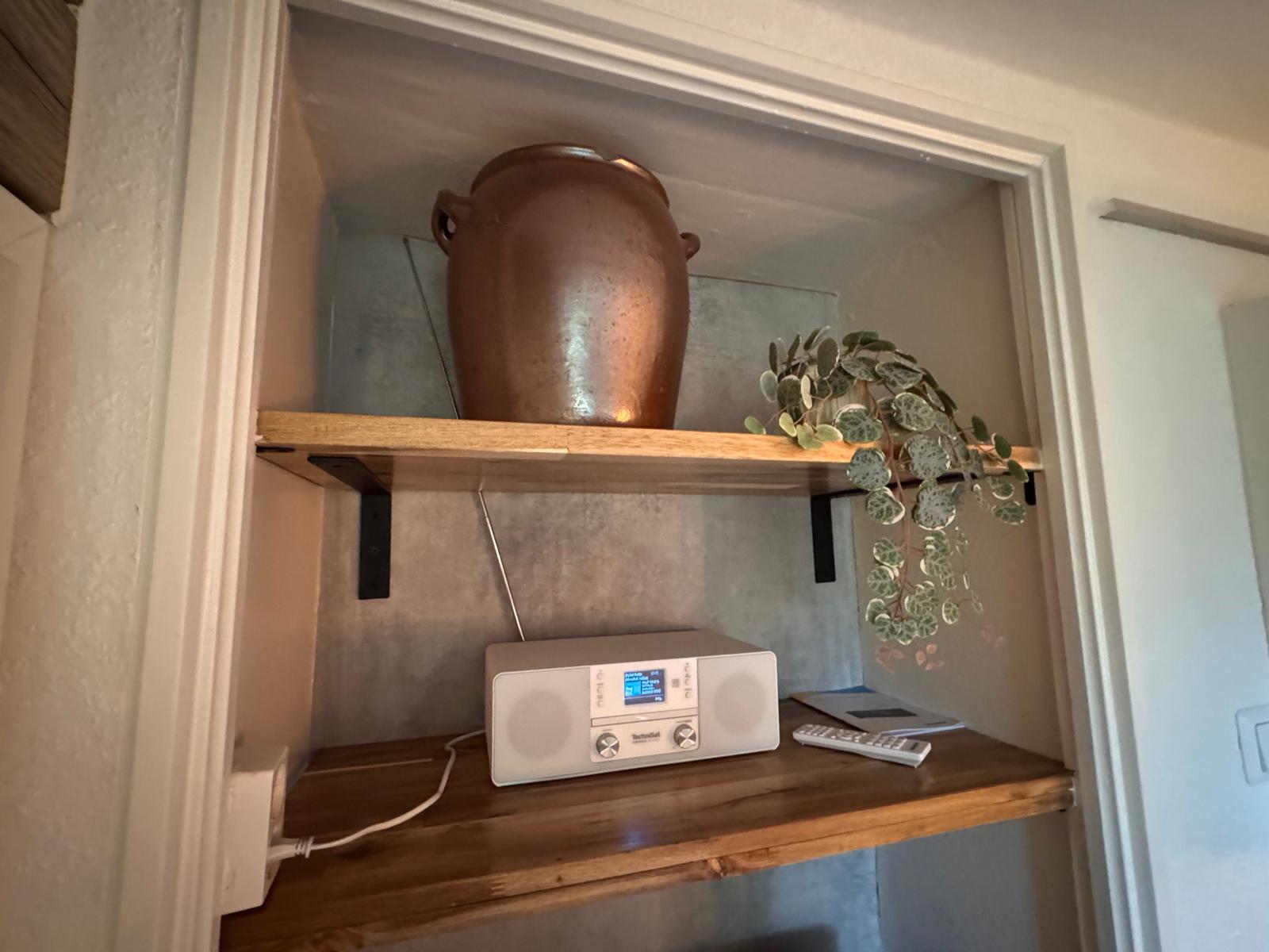 Holzregal mit Terrakottavase, Pflanze und Radio.
