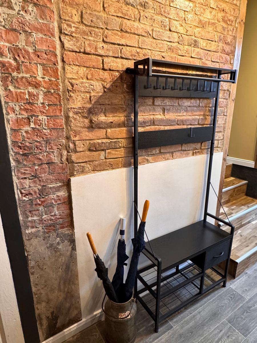 Schwarzer Garderobenstuhl vor Backsteinwand mit Regal und Schublade.