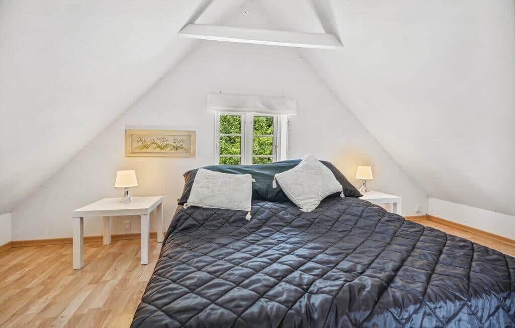 Bedroom with sloped ceiling, bed, two nightstands, and window with view of greenery.