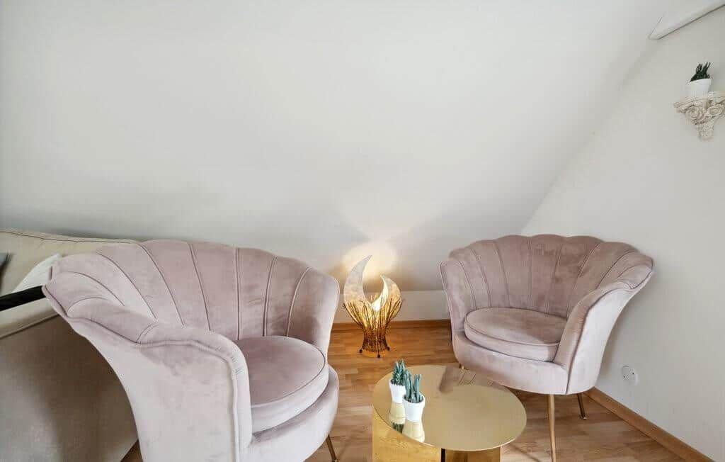 Two pink chairs and a round table are in the room with wooden floor.