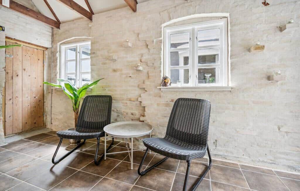 Two chairs and a table are positioned by a window in a room with stone wall and wooden beams.