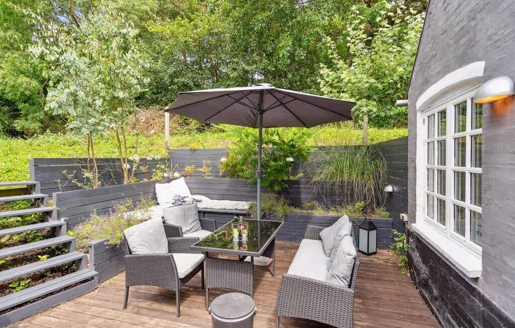 Terrace with seating group, umbrella, and plants. Wooden terrace beside house wall.