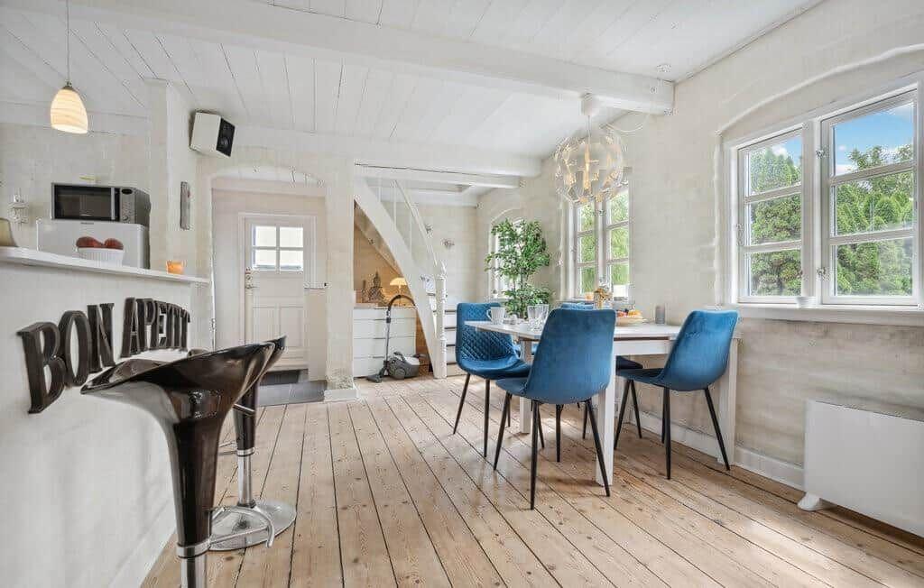 Dining area with blue chairs and wooden floor. Kitchen with bar and windows.