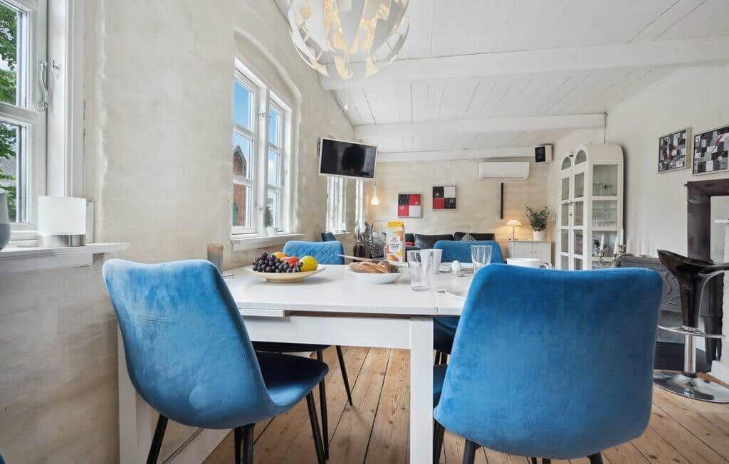 Dining area with blue chairs and white table. Wooden floor and windows visible.