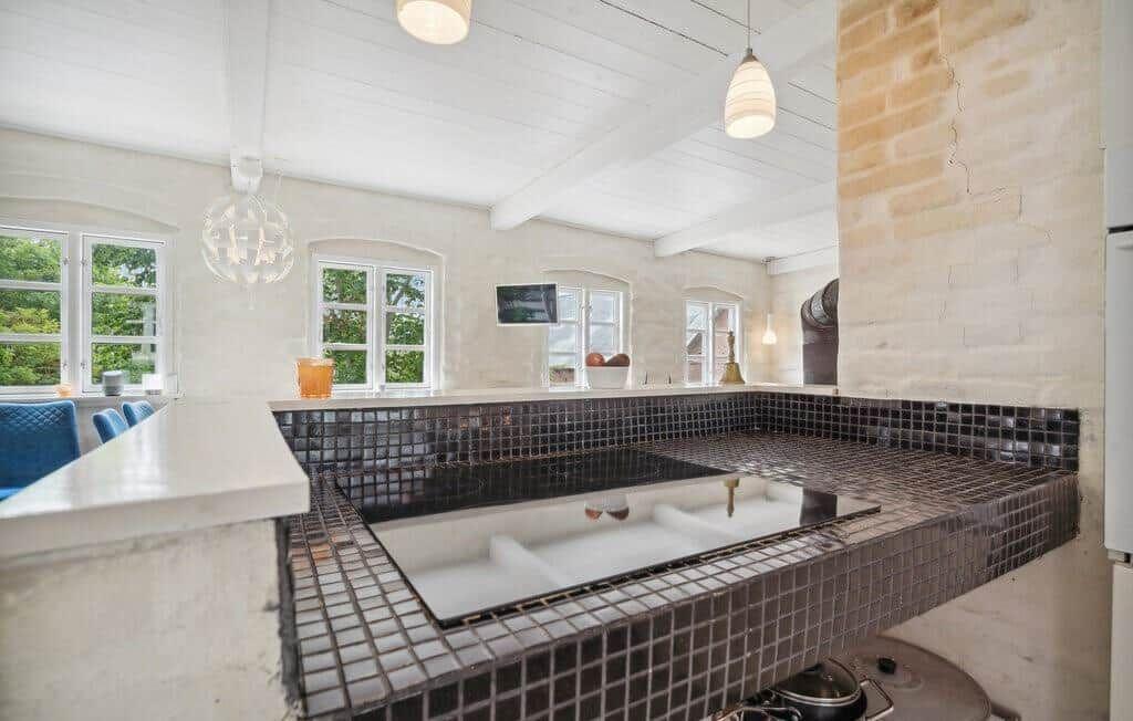 Kitchen with dark mosaic tiles and white worktop. Windows with view of greenery.