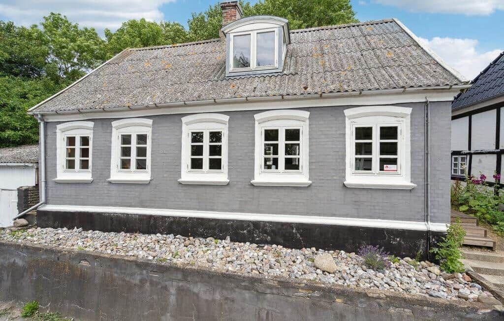 A gray house with white windows and a skylight. Surrounded by greenery and stones.