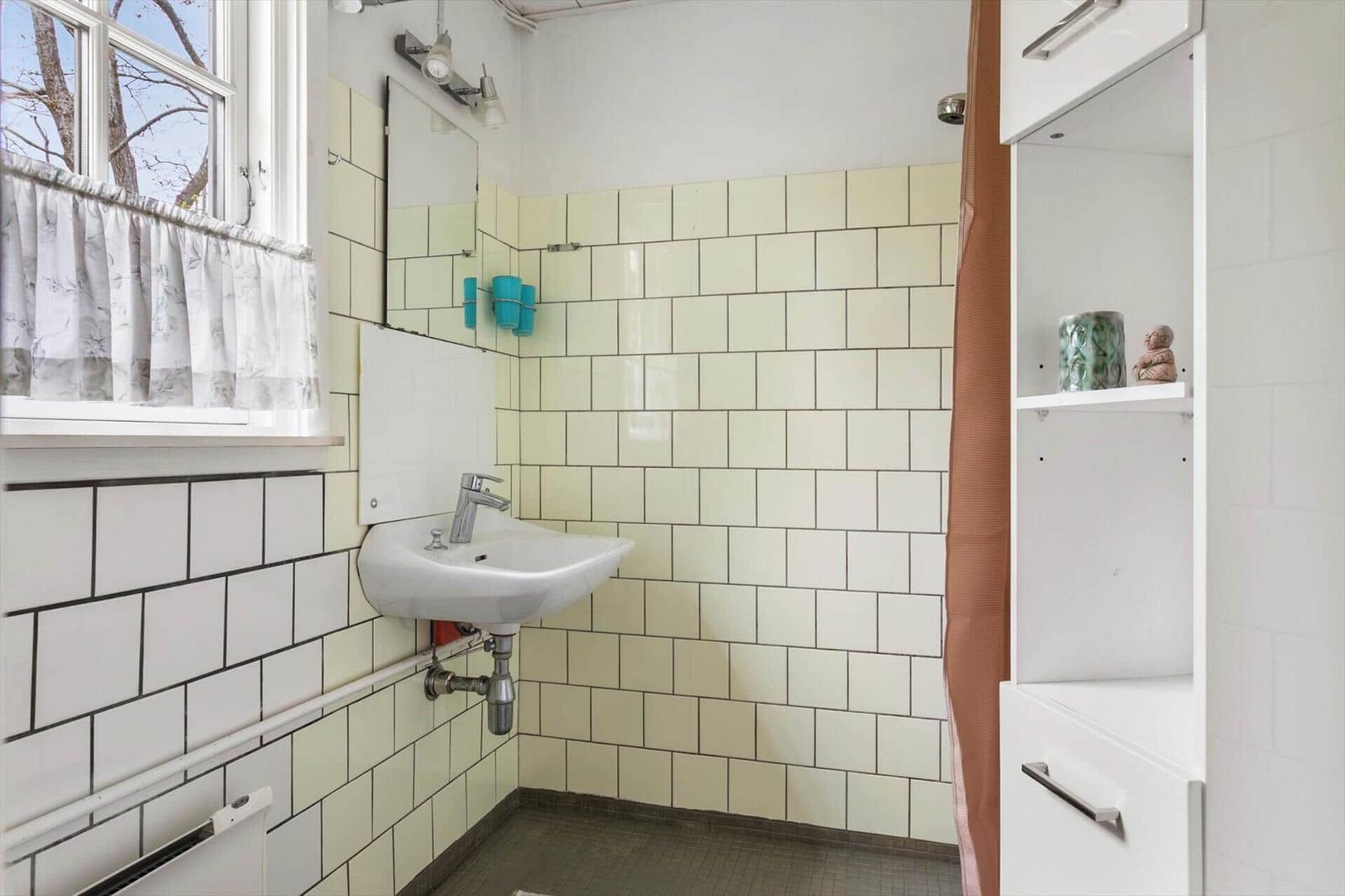 Bathroom with sink, mirror, and window. Wall tiles and cabinet visible.