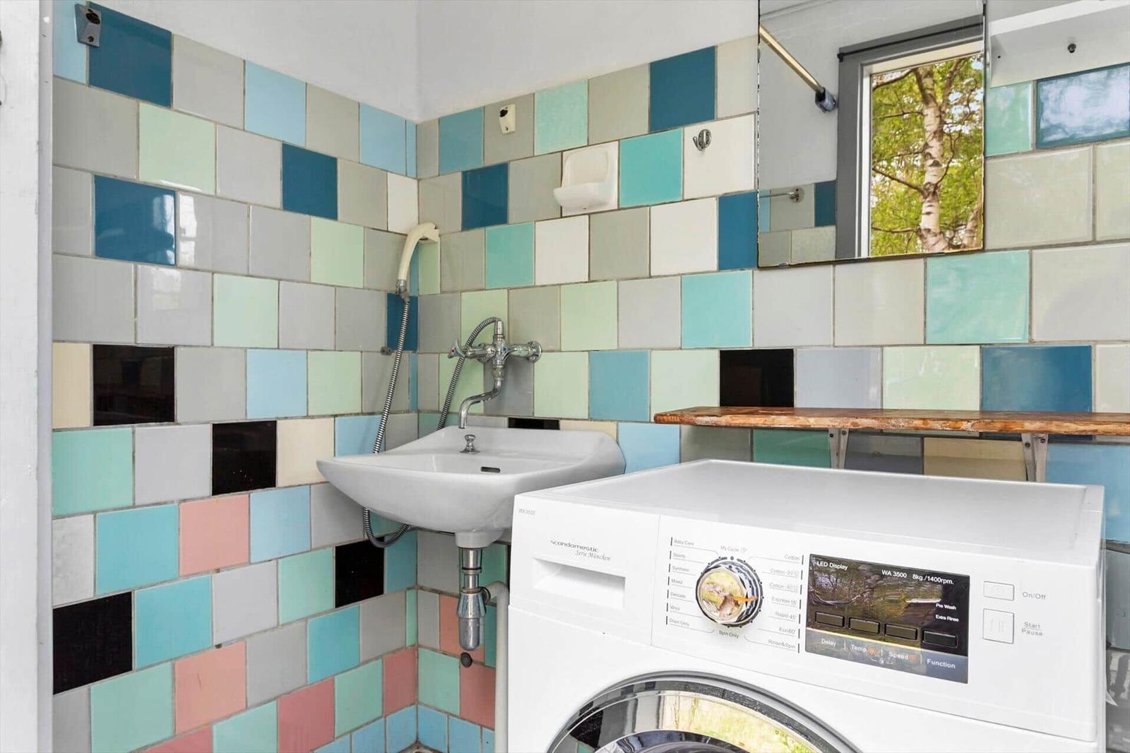 Bathroom with washing machine and colorful tiles on the walls.