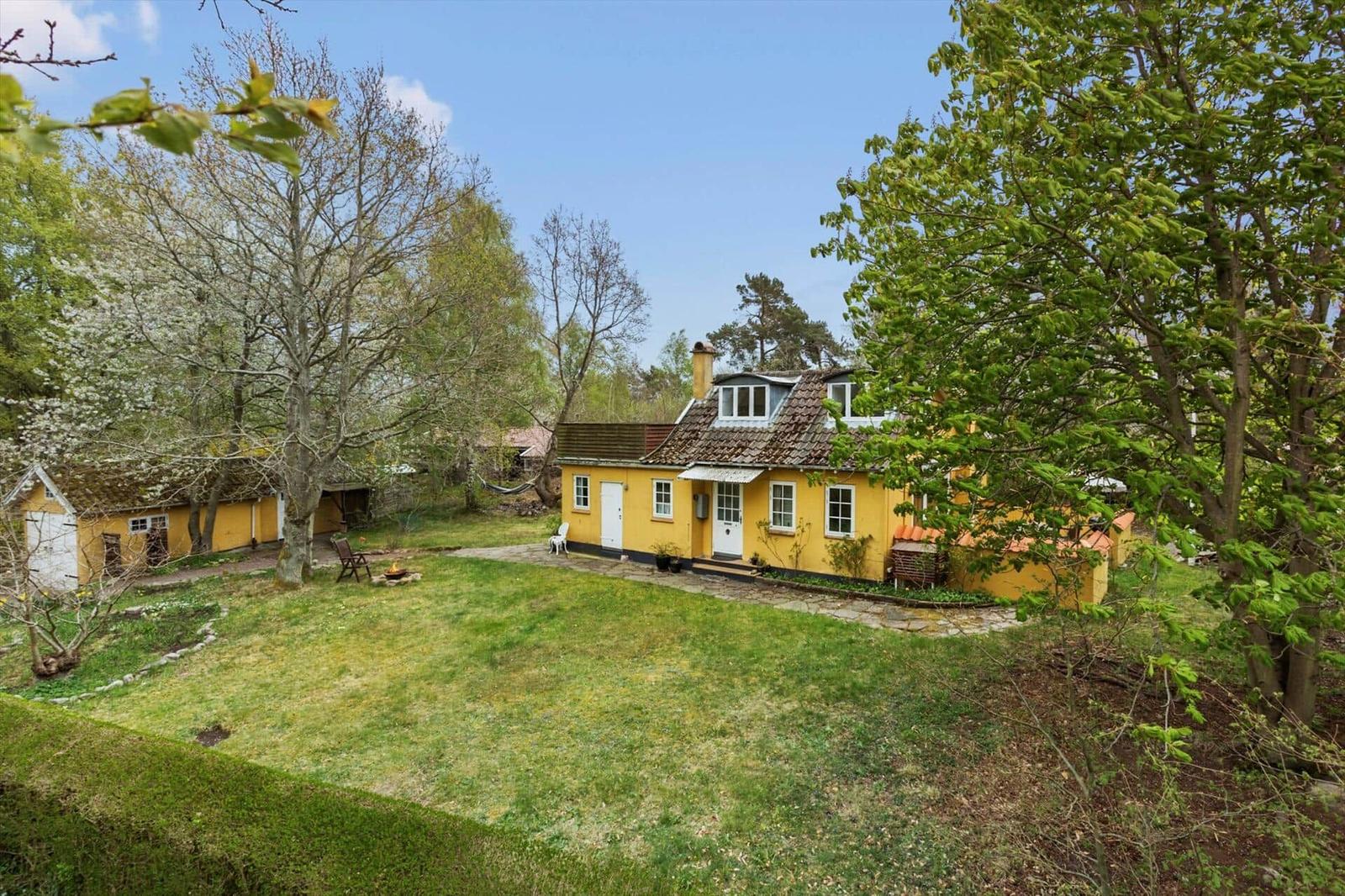 Yellow house with garden and trees under blue sky.