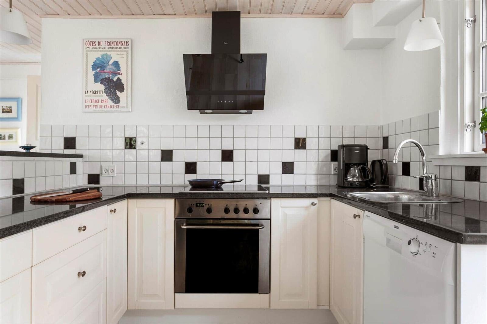 Kitchen with white cabinets, dark countertop, and oven. Wall with tiles and poster.