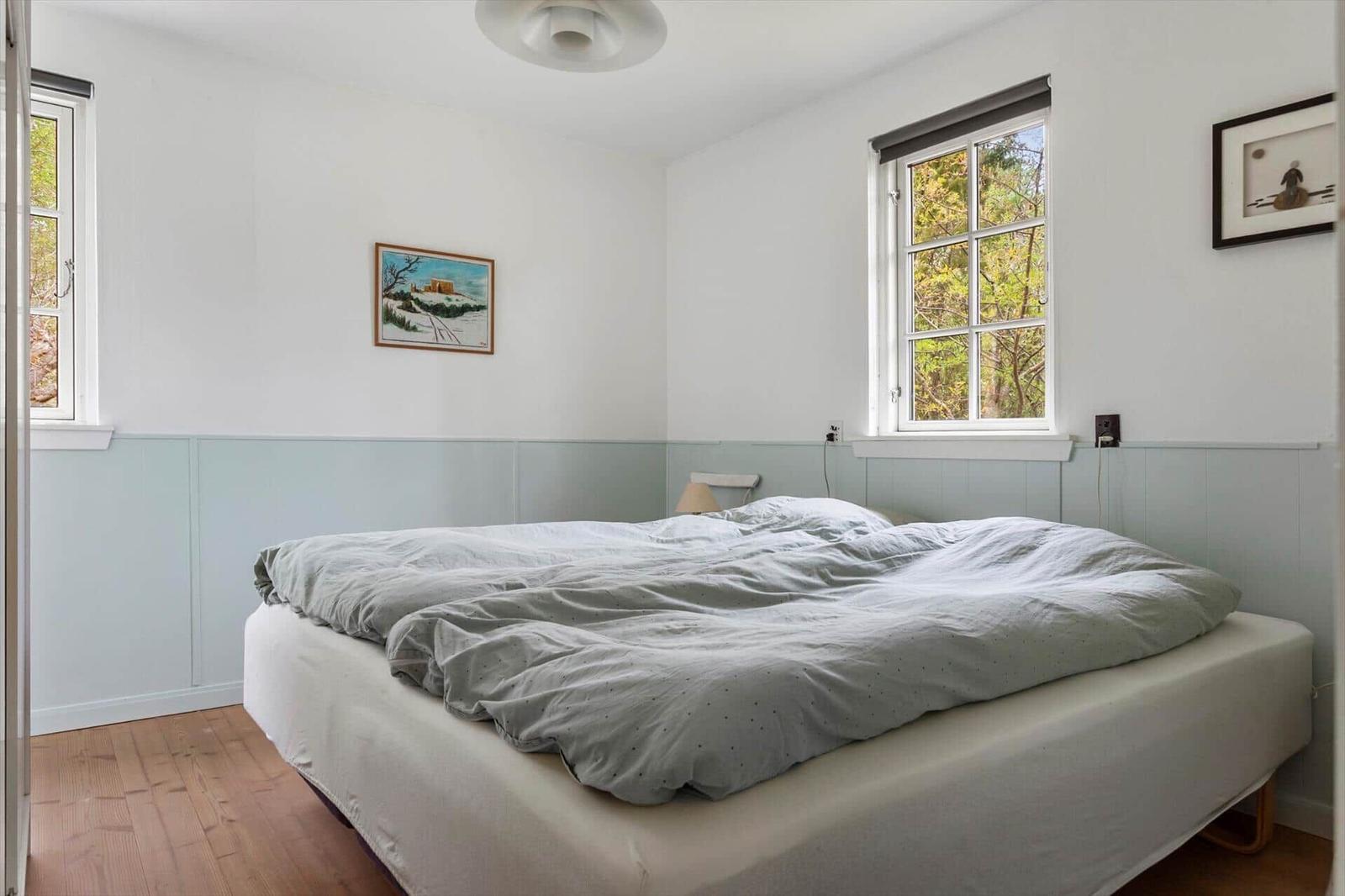 Bedroom with bed, two windows, and wall pictures.