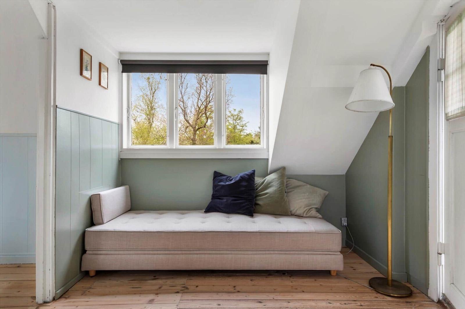 A bedroom with a sloped ceiling, window, and sofa with cushions.
