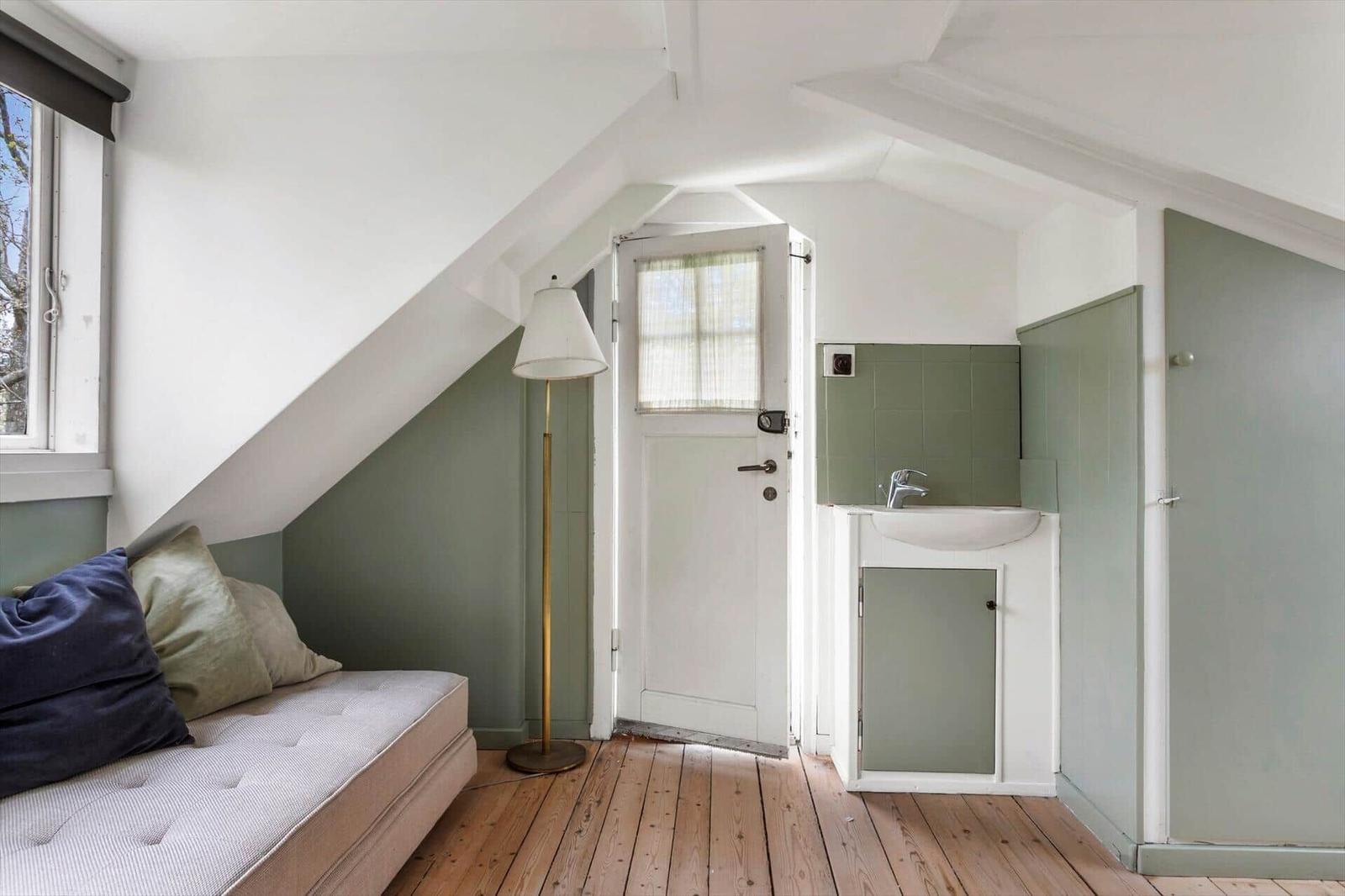 Room with bed, window, standing lamp, and small wash area with sink.