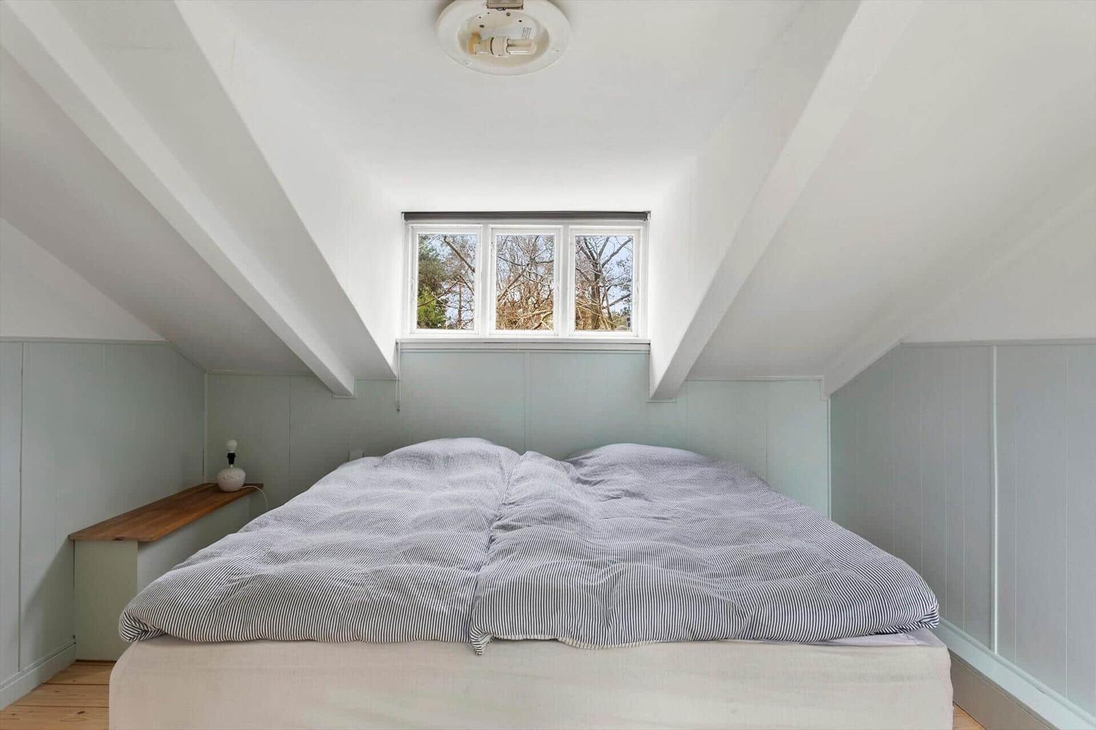 Bedroom with sloped ceiling, window, and bed with striped bedding.
