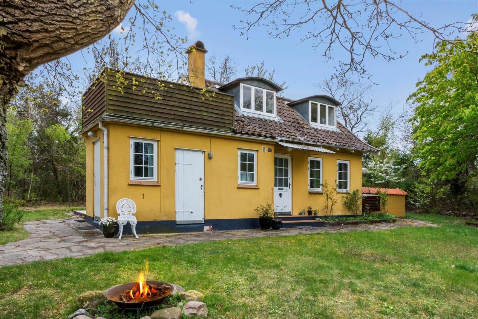 Yellow house with dormer windows and garden. A fire pit burns in the foreground.