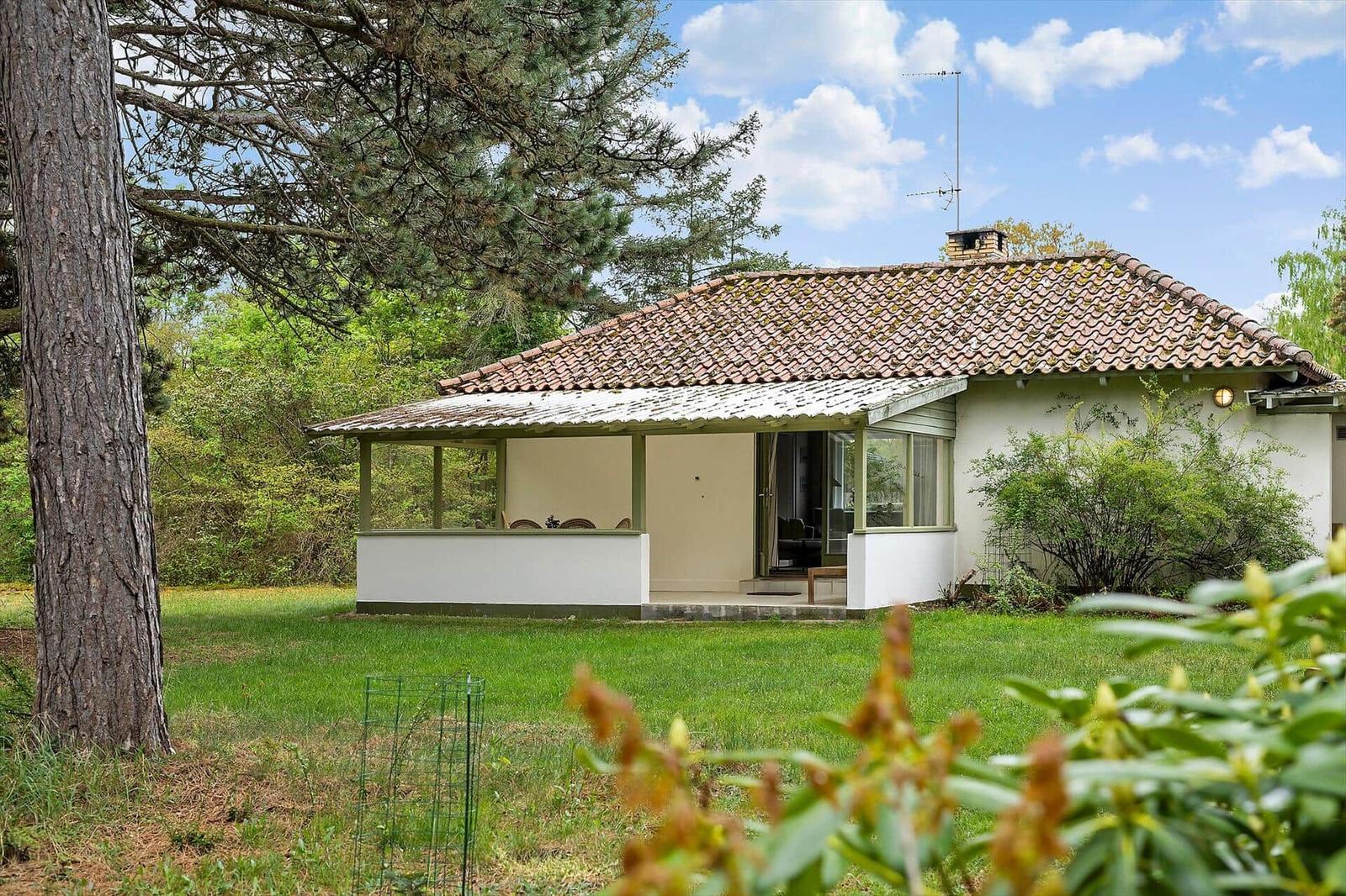 House with terrace, green lawn, and tiled roof under blue sky.
