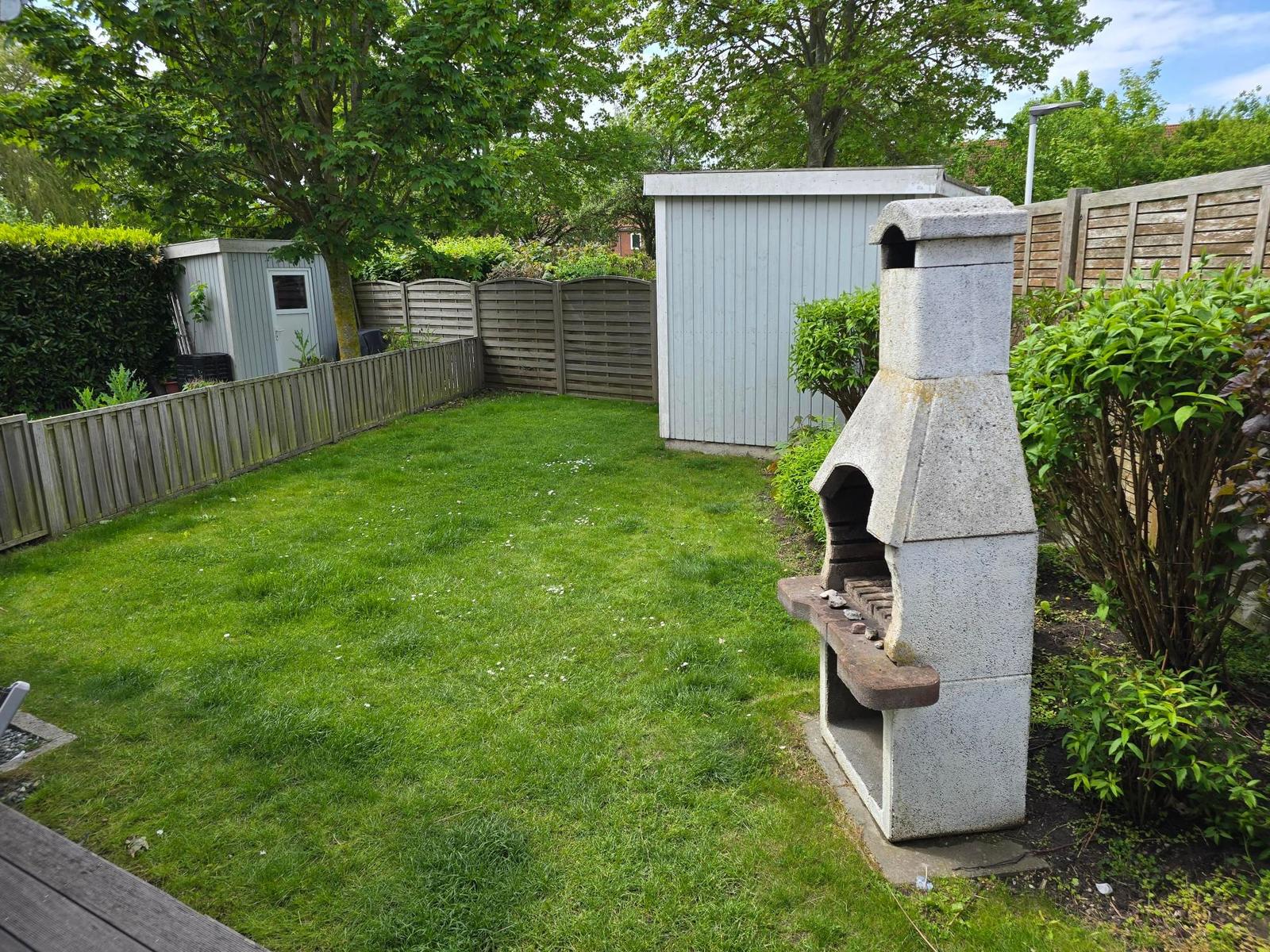 Hinterhof mit Grill, Rasen und Holzzaun. Kleiner Garten mit Pflanzen und Schuppen.