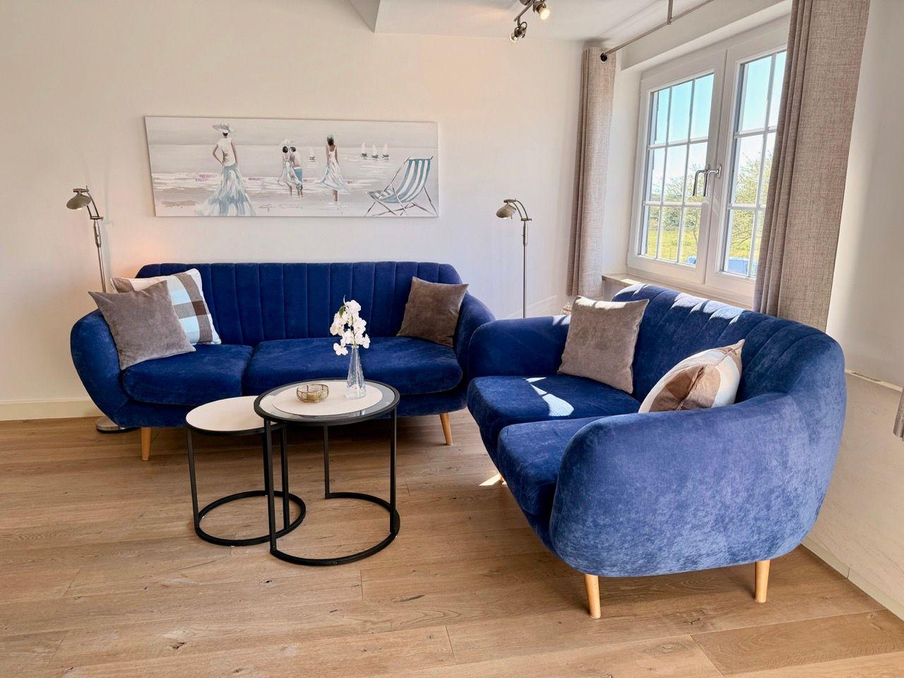 Ein Wohnzimmer mit blauem Sofa, zwei Tischen und Fenster mit Blick nach draußen.