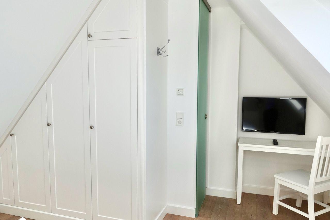Schlafzimmer mit Kleiderschrank, Schreibtisch und Fernseher unter Dachschrägen.