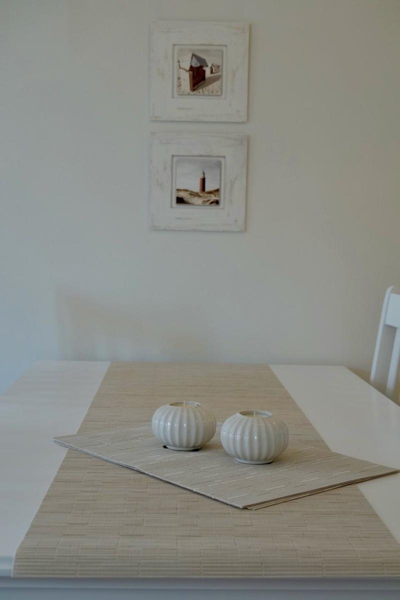 Tisch mit Bambusmatte und zwei weißen Kerzenhaltern. An der Wand hängen zwei gerahmte Bilder.