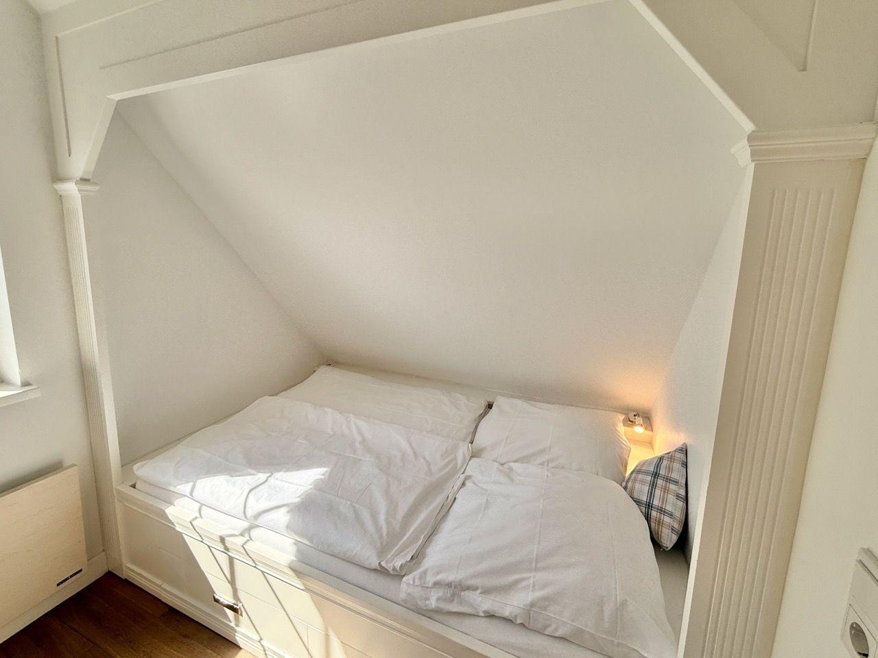 Doppelbett unter Dachschräge mit weißer Bettwäsche und Wandlampe.