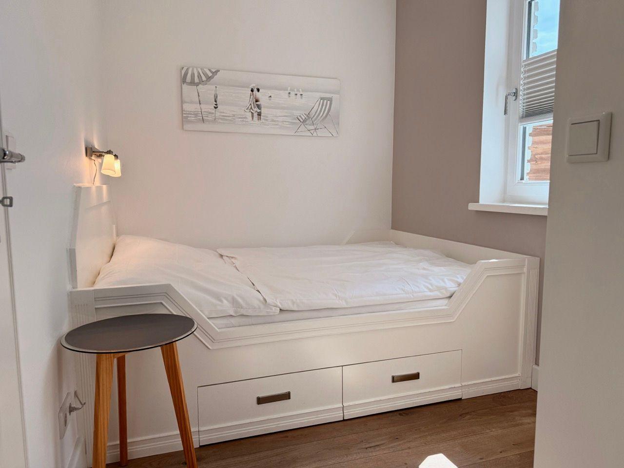 Schlafzimmer mit weißem Bett, kleiner Tisch und Wandbild.